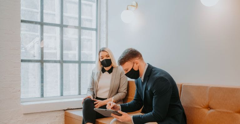 Two business professionals in masks collaborating on a project on an iPad.