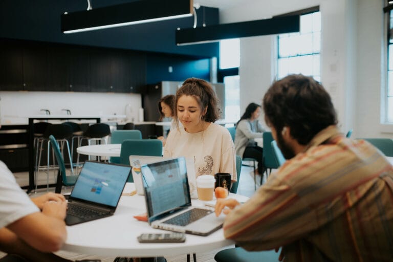 Woman sitting at a table with two other men working on something on their laptops.